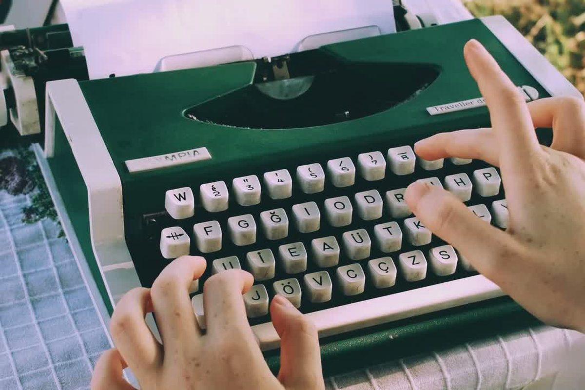 Manos de una mujer escribiendo en una máquina de escribir verde